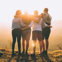 photo of four people standing on a cliff at sunset with arms around each other