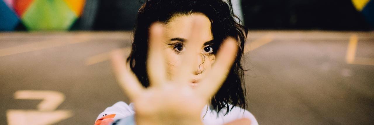 Let's Break Down These 5 Common Myths About Mental Illness A young white woman standing outside with her hand out in front of her face, indicating "stop"