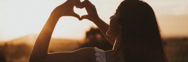 photo of a woman at sunset in a field and making a heart shape with her hands