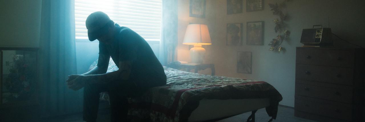 When Depression Lasts For Weeks Without End photo of a man sitting hunched over on a bed in a gloomy room