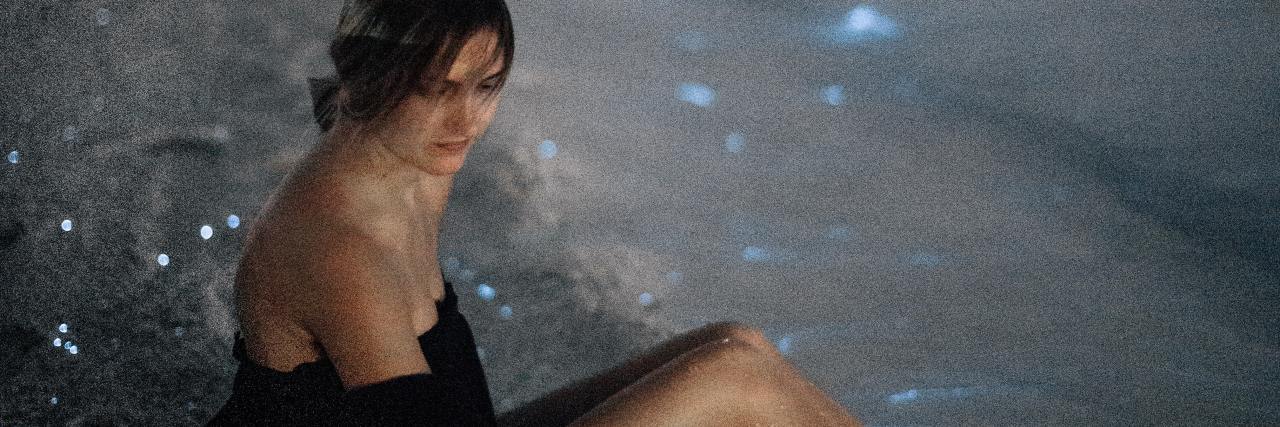 How to Cope and Build Resilience Between Trauma Therapy Sessions photo of a woman sitting on a beach with bioluminescent plankton in waves