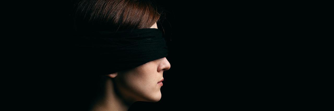 photo of a blindfolded woman standing in profile view in low light, no expression