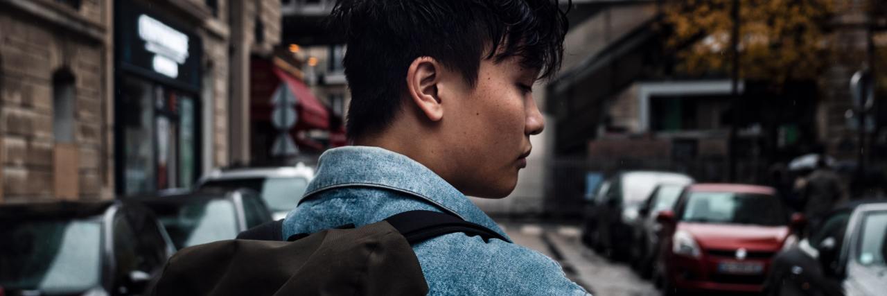 photo of a young asian man looking back over his shoulder on a street, toward camera