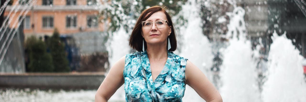 Learning to Focus on Myself Instead of My Diagnoses A proud middle-aged white woman standing in front of a fountain with her hands on her hips