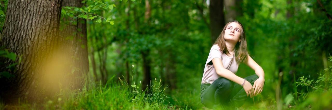 Woman crouched outside surrounded by green trees