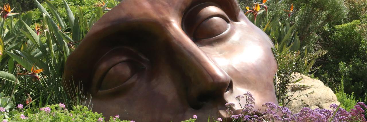 A broken ceramic mask sitting in a field, close up.