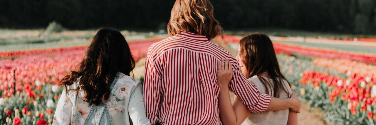 photo of three women in a flower field, supportive, one with her arm around another