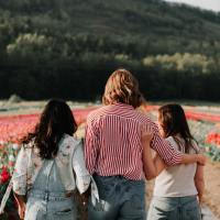 photo of three women in a flower field, supportive, one with her arm around another