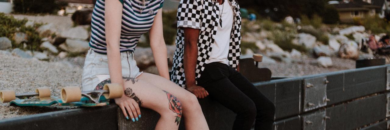 How to Start a Conversation to Help a Friend With Mental Illness A young white woman and Black woman sitting on a ledge with their legs dangling talking