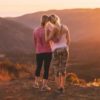 photo of two women embracing on hills while watching sunset