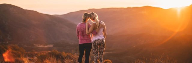 photo of two women embracing on hills while watching sunset