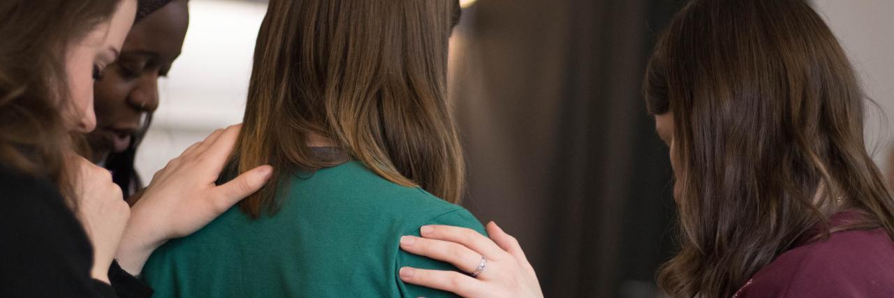 Saying 'I'm Glad You're Here' Can Help Someone Who Is Suicidal photo of multiple women standing together being supportive with hands on one woman's shoulders