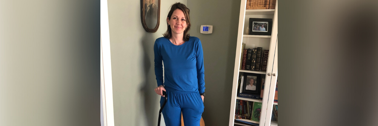 Photo of the contributor standing at home with a cane, smiling at the camera