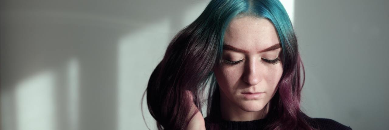 A young white woman with blue and purple hair looking down sad