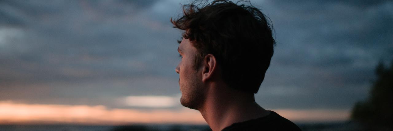 A young white man with short brown hair looking out at an ocean at sunset