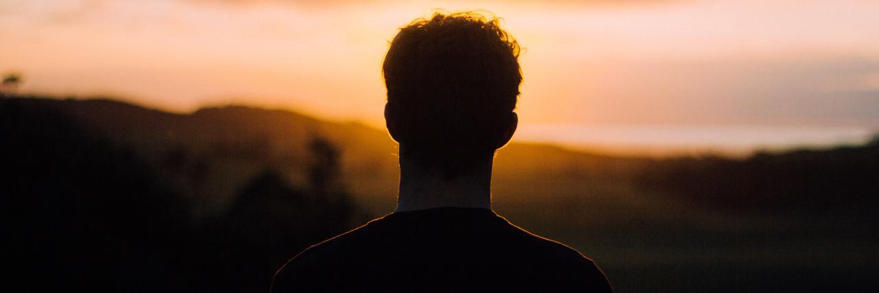 Back of a young man standing on a mountain during the sunset