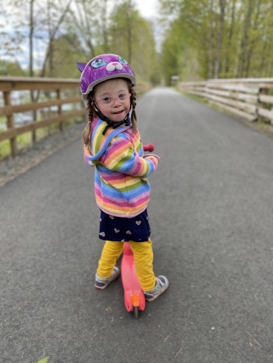 Lily wearing a rainbow striped shirt and purple helmet.