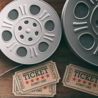 Film reels with retro cinema tickets, movie clapper and red theater seats on wooden background.