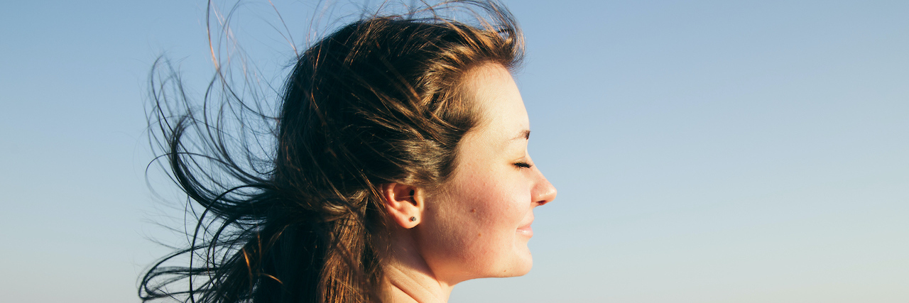 Woman with dark hair faces the ocean with her eyes closed