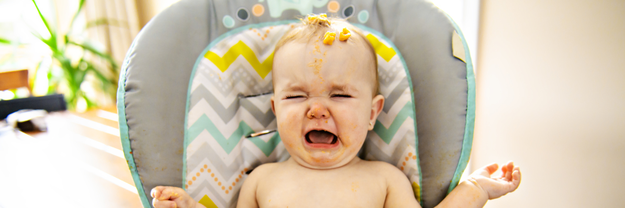 a toddler girl crying in high chair eating