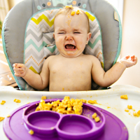 a toddler girl crying in high chair eating