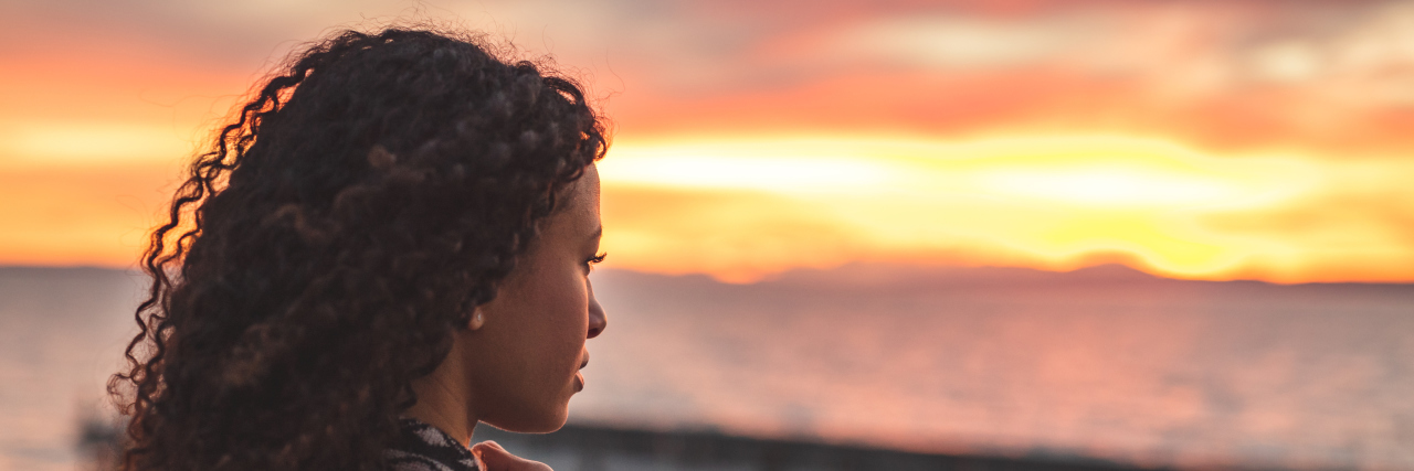 Adapting Self-Talk and Affirmations for Life With Chronic Illness Black woman with long curly hair looking at the sunset.