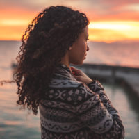 Black woman with long curly hair looking at the sunset.