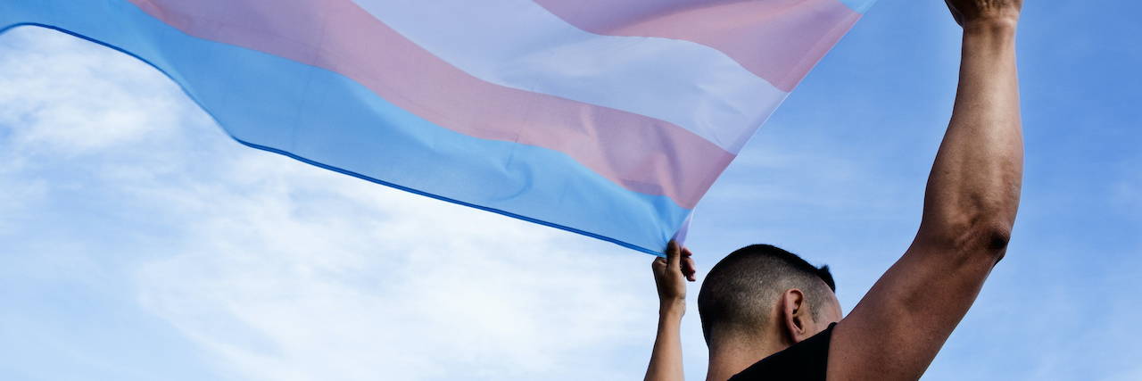 A young man holding a transgender flag over his head