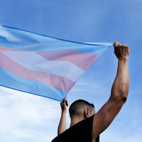 A young man holding a transgender flag over his head