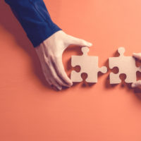 Two hands each holding a jigsaw puzzle piece next to each other