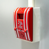 Red fire alarm switch on concrete wall in office building.