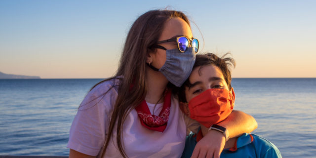 Mother and son wearing masks by the ocean.