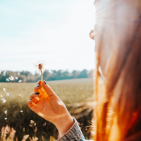 a woman is blowing a dandelion in a field