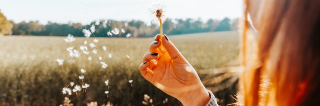 a woman is blowing a dandelion in a field