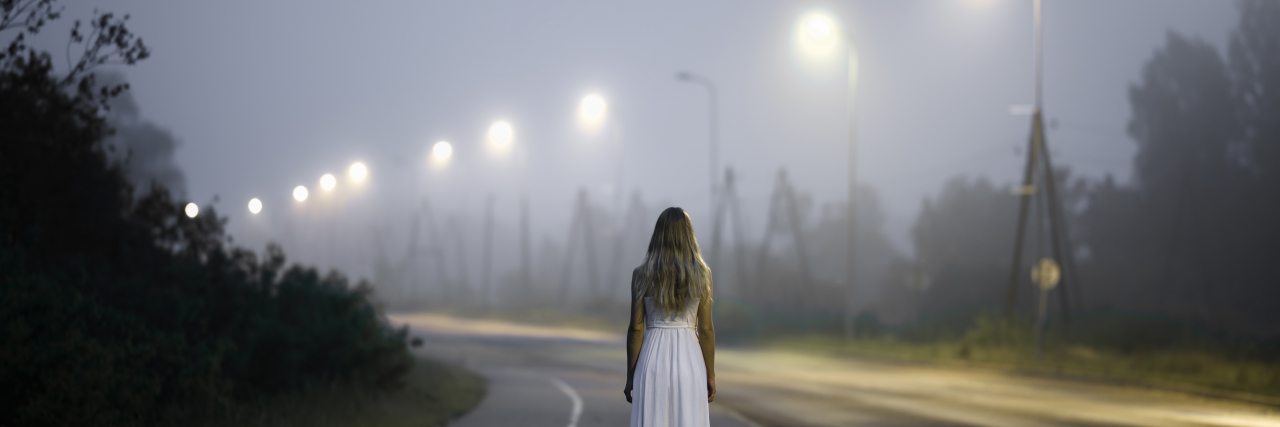 28 People With Chronic Illness Explain What ‘Brain Fog’ Feels Like to Them woman in white dress walking alone on a dark street