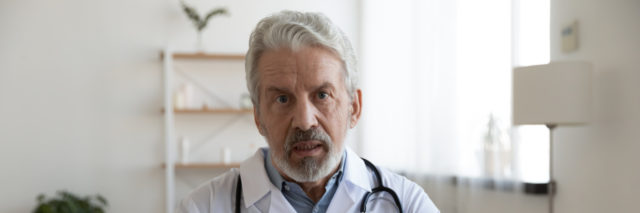 Doctor wearing white coat with stethoscope looking serious.