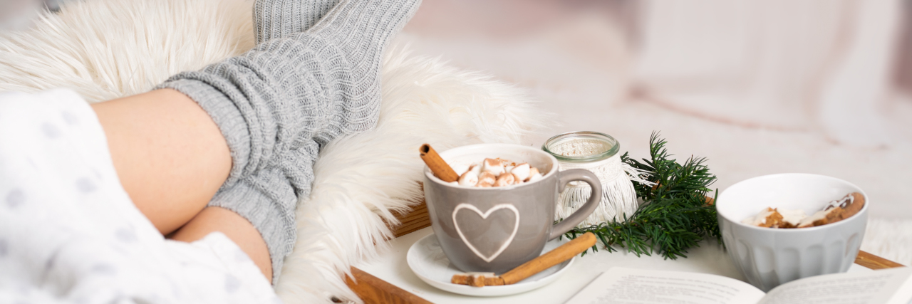 Redefining a Meaningful Life With Chronic Illness woman on sofa with a book and hot chocolate.