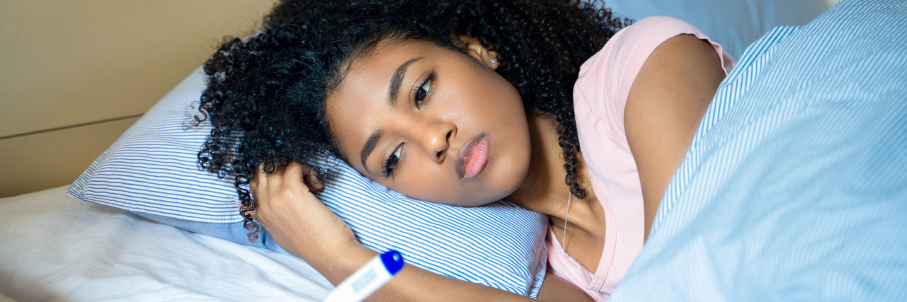 A young black woman lying in bed sad, looking at a pregnancy test
