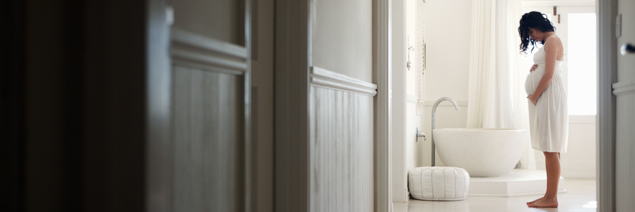 The Maternal Mental Health Struggles We Aren't Discussing pregnant woman standing in a white bathroom