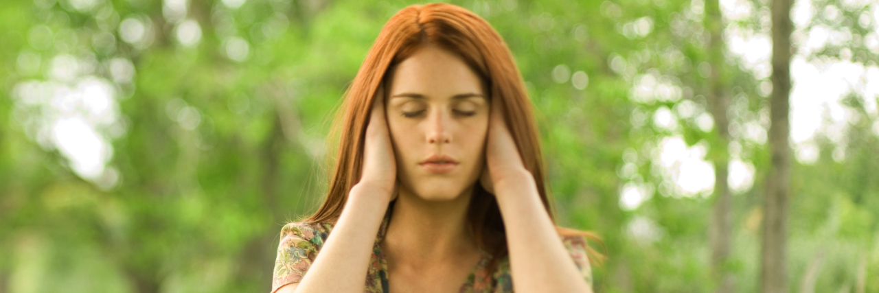 Woman with hands over ears and eyes shut, outdoors