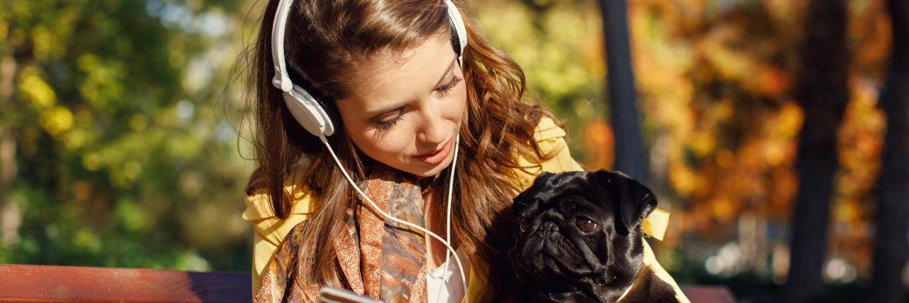 a young woman with headphones sitting with a black dog