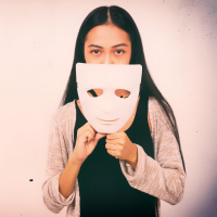 Woman holding theatre mask near her face.
