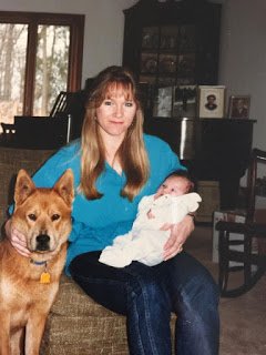 Photo of contributor as a baby being held by her mother, next to a dog