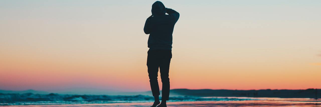 How to Cope on Days Your Inner Critic Is Too Loud photo of a man at sunset on a beach with his reflection in the still water