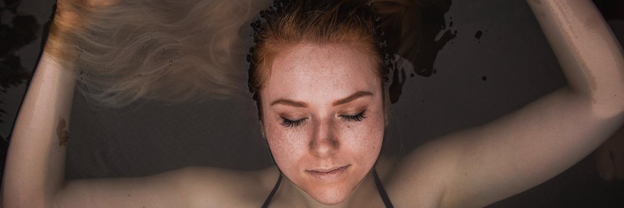 How Flotation Therapy Helps My Mental and Chronic Illnesses Young white woman floating in the water with her eyes closed
