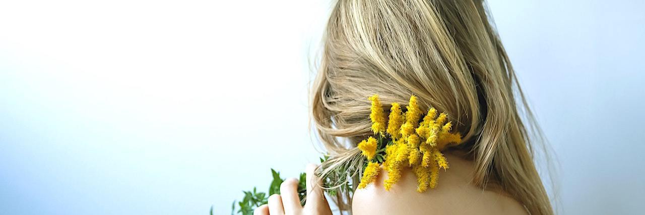 A List of 15 Concrete Ways to Re-Mother Yourself A woman holding a flower over her shoulder