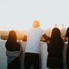 A group of friends with their back to the camera standing over a ledge that looks over a city at sunset