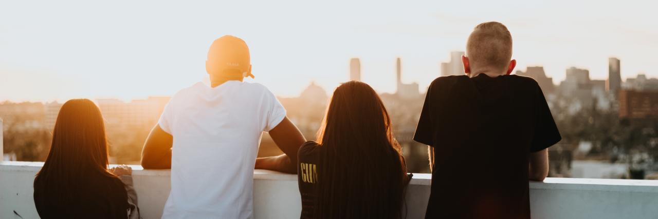 How to Adjust to Life After the Stress and Trauma of COVID-19 A group of friends with their back to the camera standing over a ledge that looks over a city at sunset