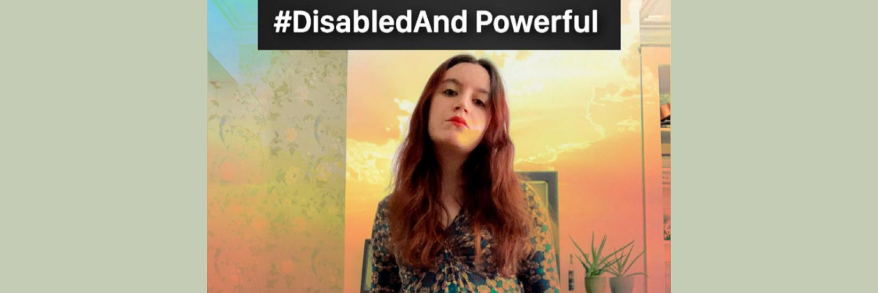 Photo of Sophia a white woman with brown and red hair wearing a blue and green geometric print dress and holding a red cane. She is looking at the camera with pride. In the background is a computer and desk and layered over the photo is a sunset scene. Above her in a black box are the words, “#DisabledAnd Powerful”.