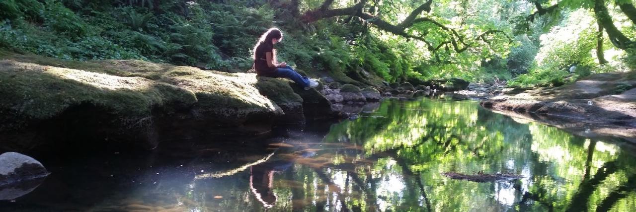 Finding Life's Purpose When You Have Several Chronic Conditions Woman sitting on rock by river looking at the reflections in the still water